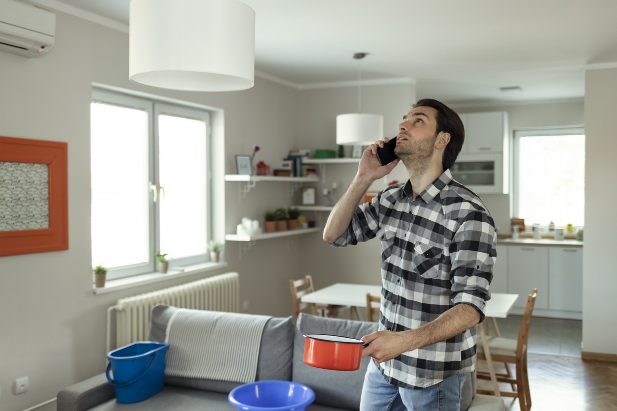 Roof Leaking Angry Men Talking on Smartphone Near Plastic Wash Bowl at Home in the Living Room Because of Roof Leaking