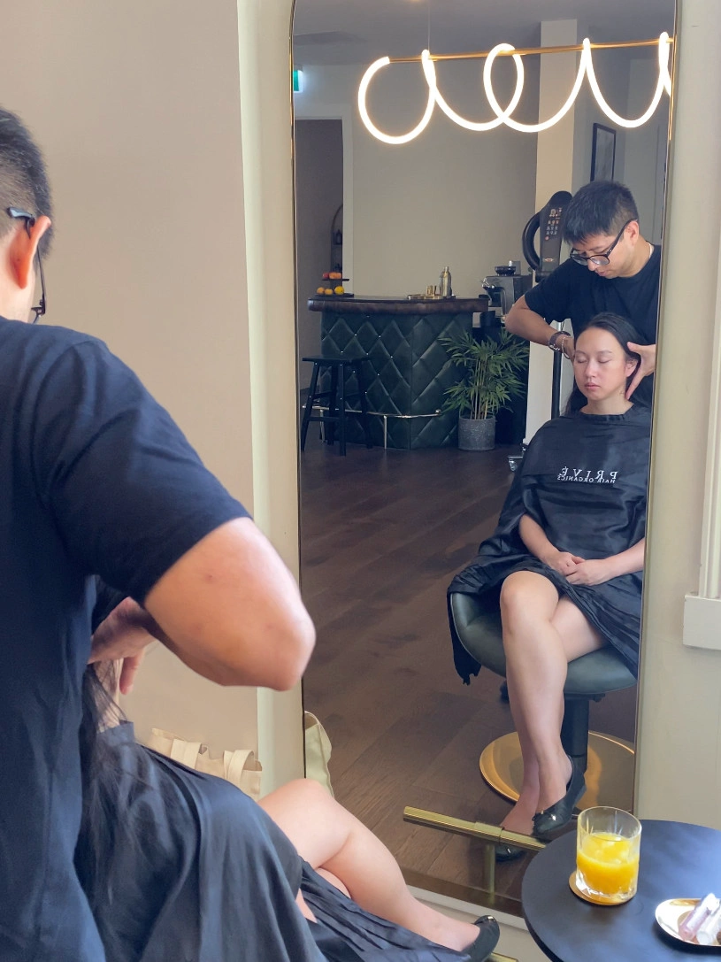 A client sits in a salon chair receiving a head massage.