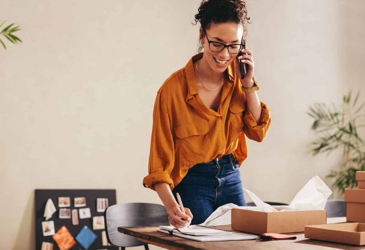 shutterstock_1840295068-scaled Female entrepreneur working at home office confirming the order on phone.