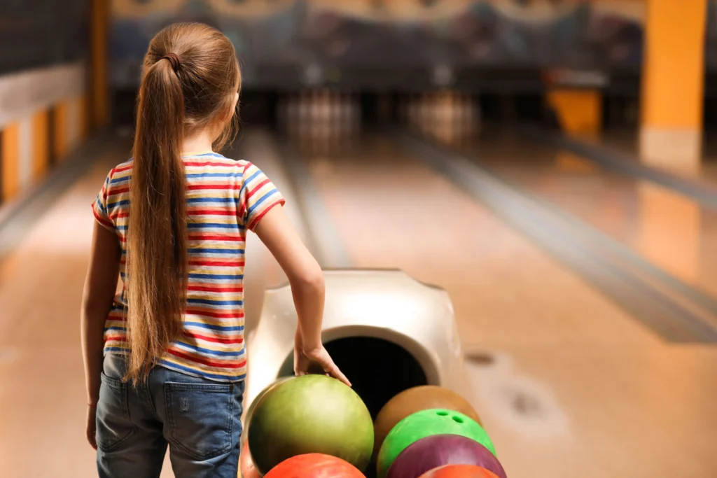 little girl picking up bowling ball at bowling alley for cheap school holiday activity | swoosh finance