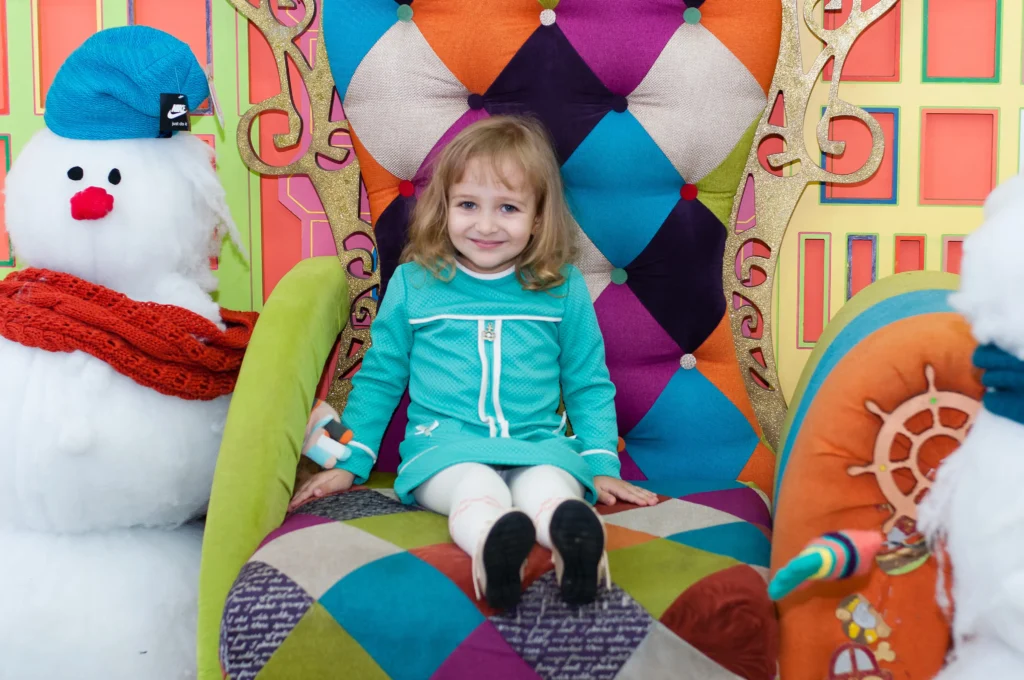 little girl smiling and sitting on a colourful Christmas chair in a shopping centre | Swoosh Finance