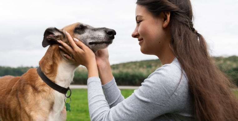 A smiling woman holds a dogs face as if to give it a kiss.