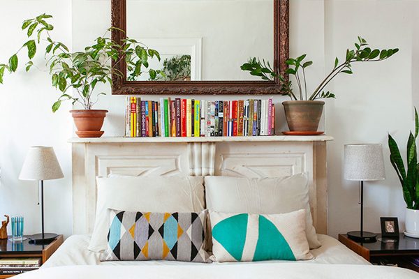an organized shelf with a line of books and plants on top, inside a bedroom
