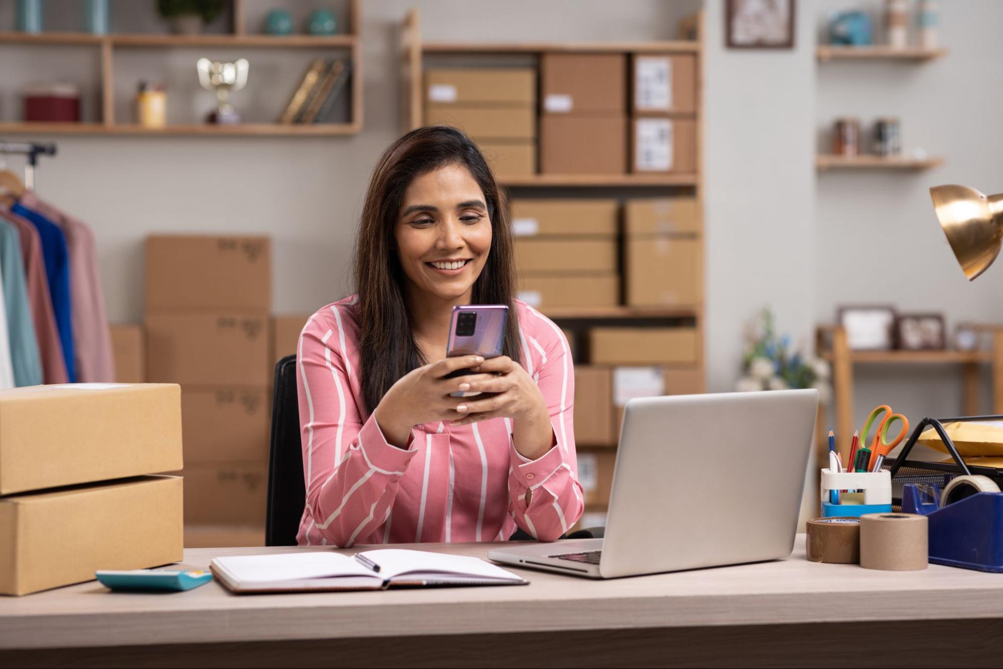 A woman working at a desk, using a laptop, with a phone beside her, illustrating a productive workspace.