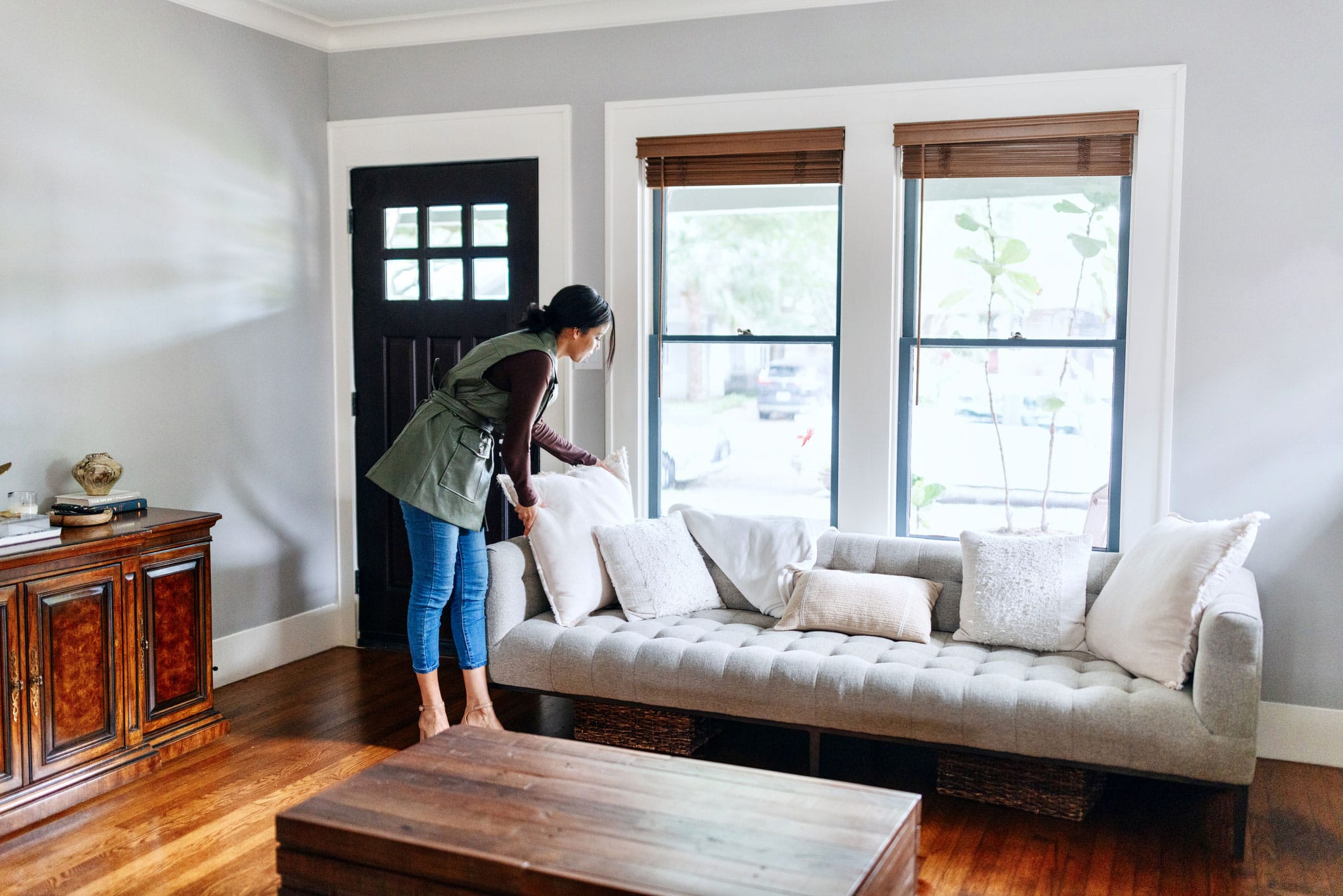 A woman stands in a living room, positioned in front of a couch, with a cozy atmosphere surrounding her.