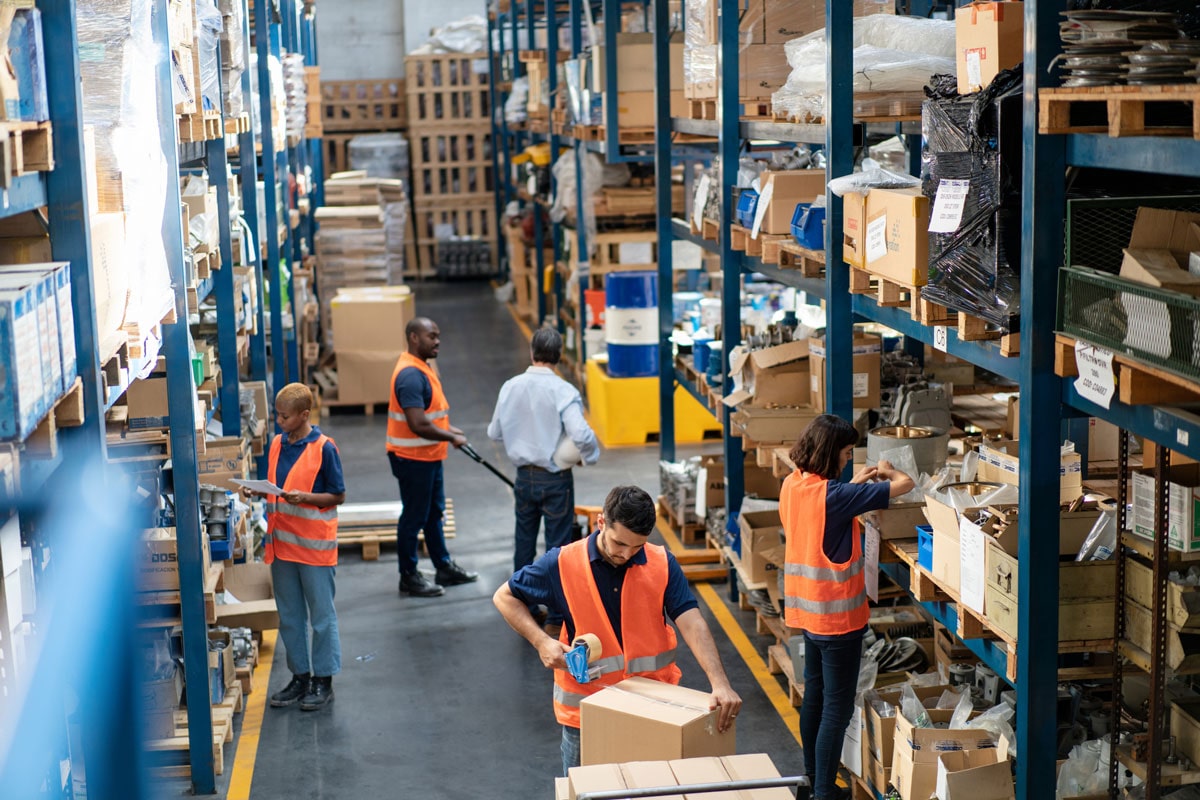 Workers organize boxes on shelves in a warehouse, showcasing mobile storage solutions for lean manufacturing efficiency.