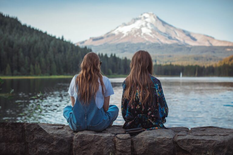 Two girls sitting on a ledge looking out towards the mountains
