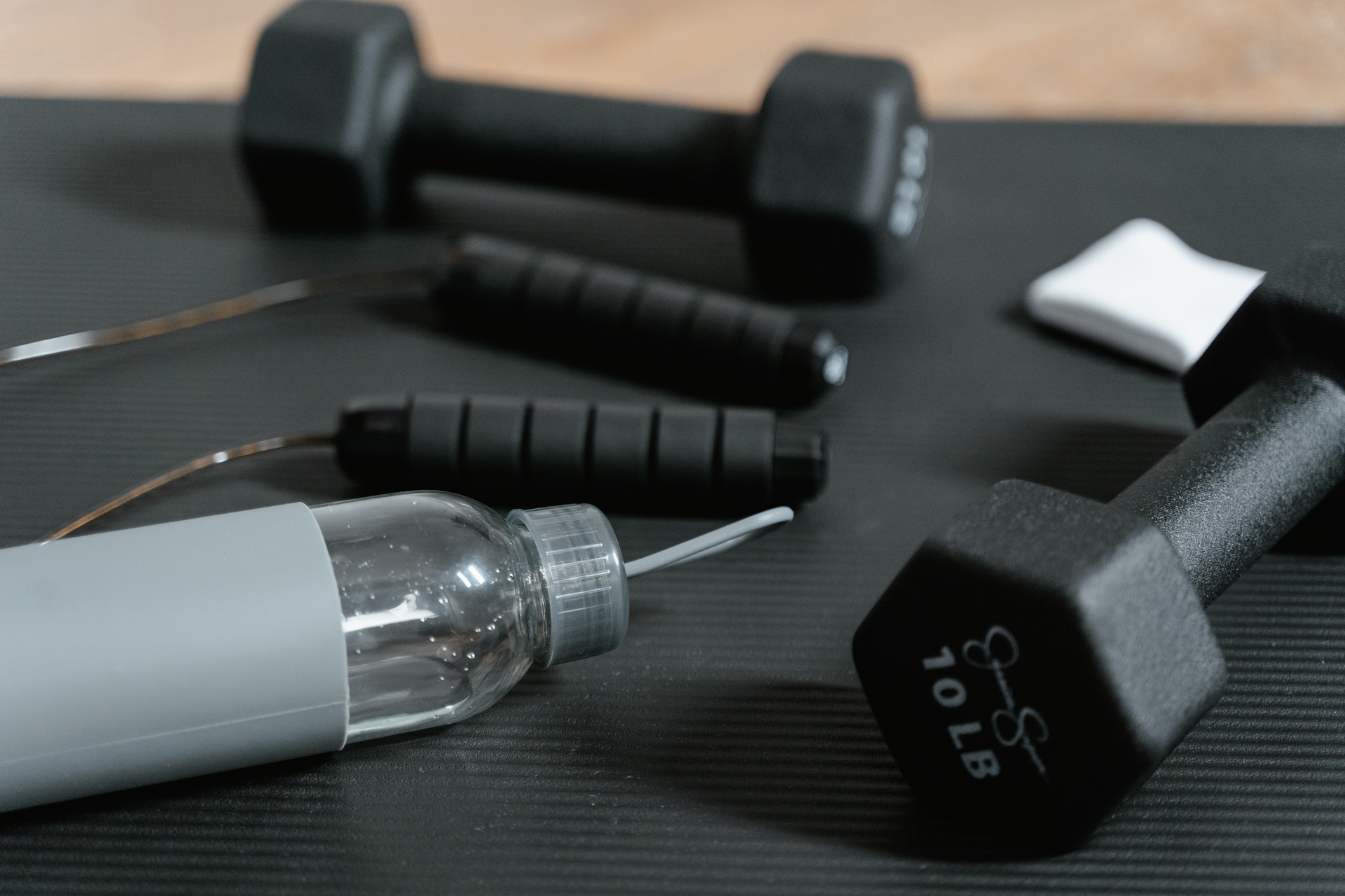 Dumbells, skipping rope and water bottle laying on an exercise mat